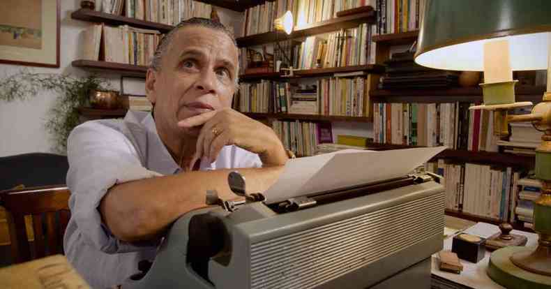 Apoiado em mquina de escrever, o ator Rodolfo Vaz olha para cima