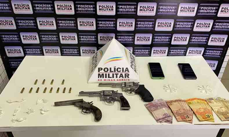 mesa com armas, munies, dinheiro, celulares e o smbolo da Polcia Militar