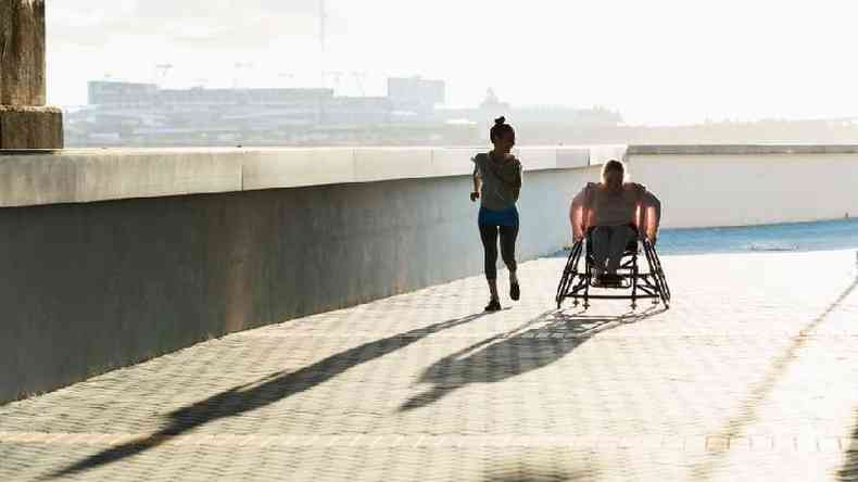 Duas mulheres treinando, uma correndo e outra em cadeira de rodas