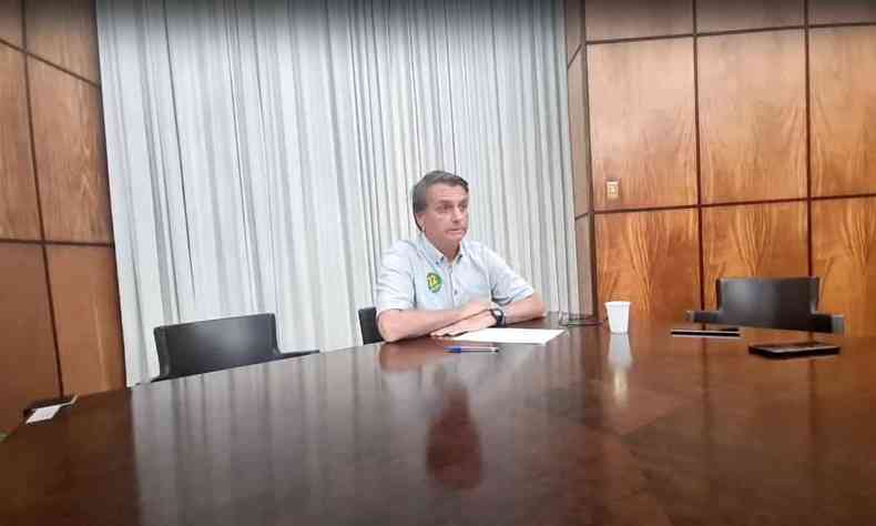 Jair Bolsonaro sentado em uma mesa sozinho durante uma live