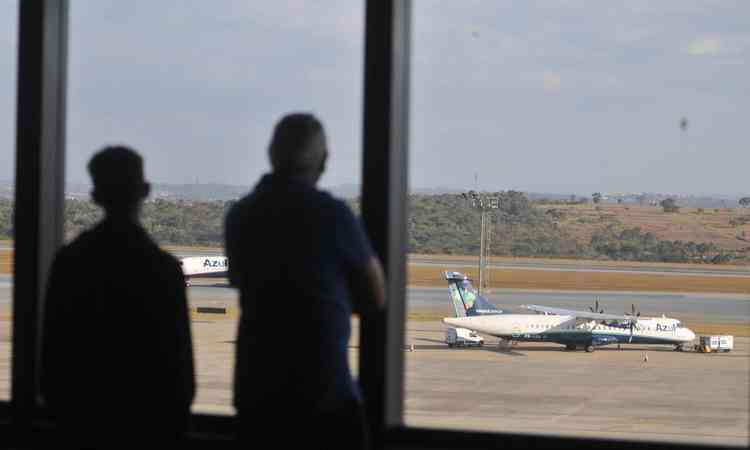 Duas pessoas olham de uma janela avio da Azul no aeroporto de Confins