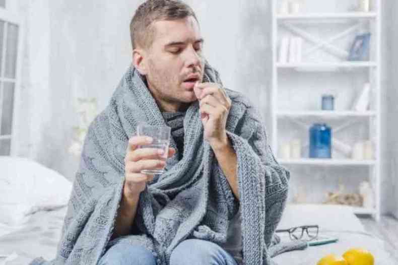 Homem envolto em cobertor tomando um comprimido