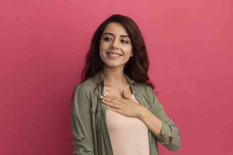 Mulher sorrindo com uma camiseta rosa e um fundo rosa escuro com a mo esquerda no peito