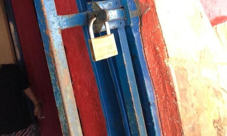 Porta com cadeado; dentro da casa  possvel ver a presena de uma mulher