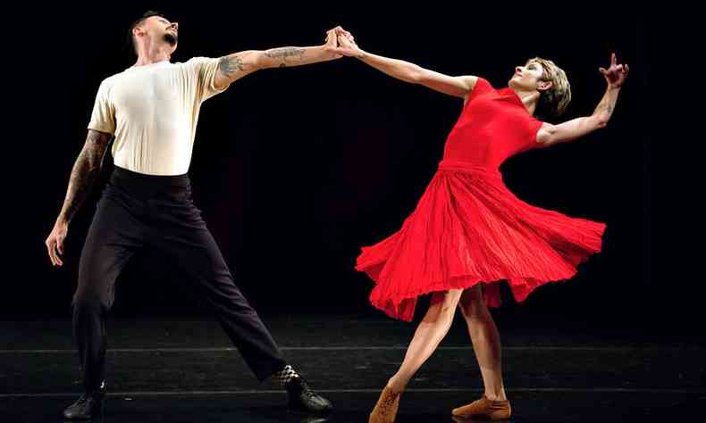 Bailarino de cala preta e camisa branca e bailarina de vestido vermelho ampliam os braos e se tocam as mos