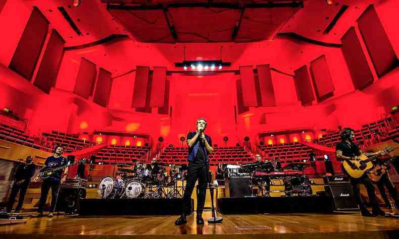 Rogrio Flausino no centro do palco da Sala Minas Gerais, vestido de preto, com fundo de iluminao vermelha 