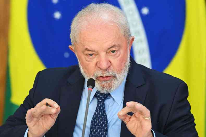 Lula, usando terno preto, camisa azul clara e gravata azul escura, fala em pulpito diante da bandeira do Brasil