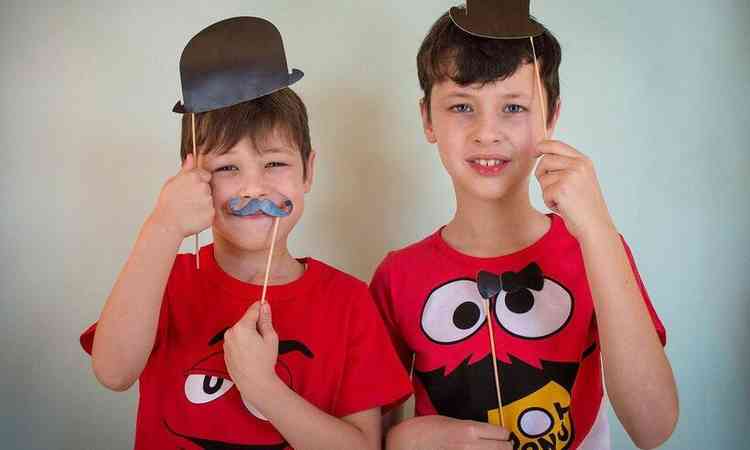 dois meninos brincando com adereços de teatro , chapéu, gravata  e bigode confeccionados de papel 