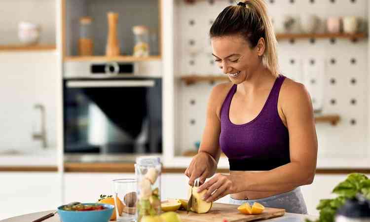 Mulher atltica feliz cortando frutas enquanto prepara uma refeio saudvel na cozinha
