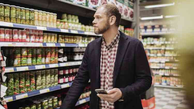 Homem no corredor de supermercado com celular na mo