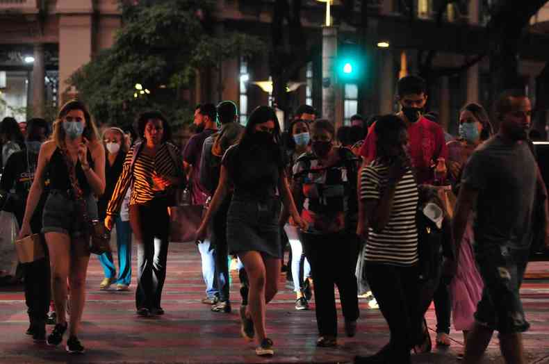 Pessoas caminham pelo centro de BH, algumas com máscaras, no início da noite