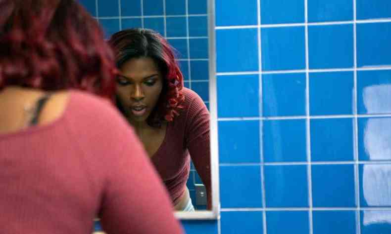 Mulher trans e negra tirando a maquiagem de frente para um espelho