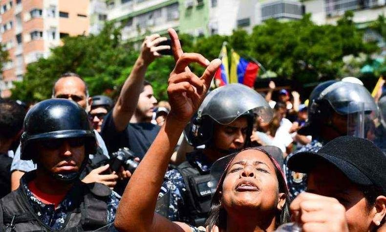 Apoiadores FR Juan Guaid� protestam diante de uma fila de oficiais da Pol�cia Nacional Bolivariana em Caracas, neste s�bado (foto: RONALDO SCHEMIDT/AFP )