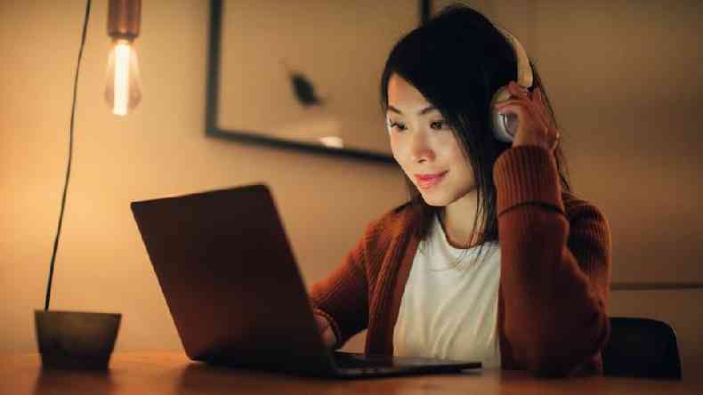 Uma mulher com fones de ouvido sentada em frente a um laptop