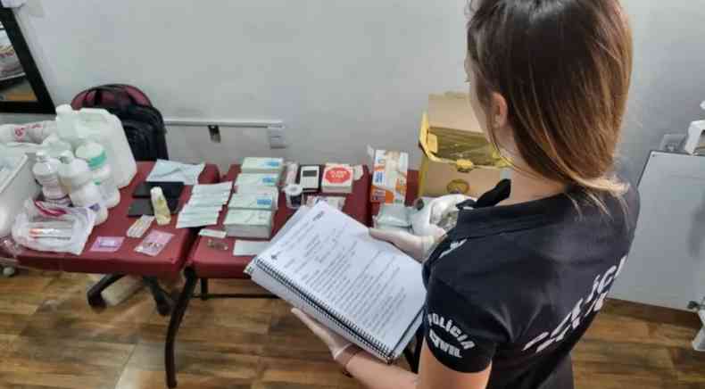 Agente da Polcia Civil fiscalizando/olhando para mesa com produtos apreendidos da cirurgi