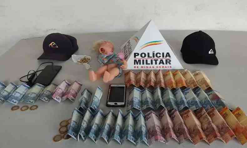 Divulgao da Policia com a droga apreendida, a boneca, dinheiro, bon e celulares em uma mesa