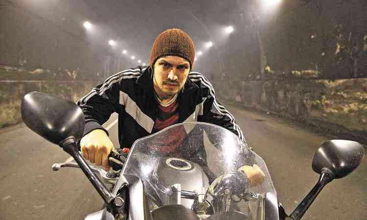 O ator Gabriel Leone, vestindo gorro e jaqueta, com expresso sria, pilota moto em cena de 'Dom'