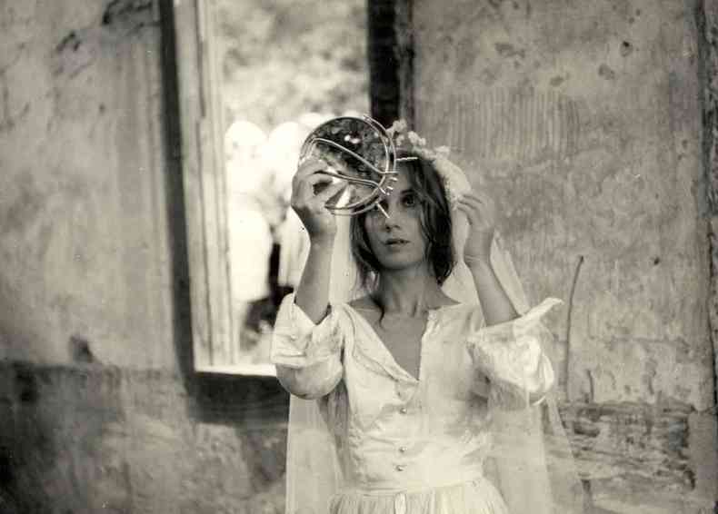 Vestida de noiva, a atriz Helena Ignez olha no espelho em cena do filme O padre e a moça