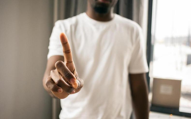 Homem negro usa camisa branca e aponta com o indicativo