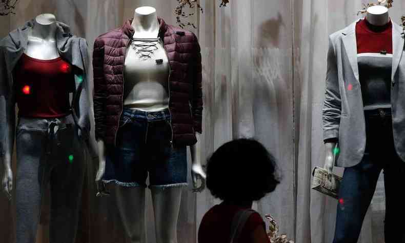Mulher observa a vitrine de uma loja de roupas com três manequins