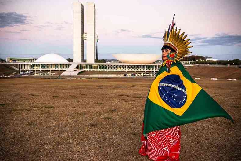 Clia Xakriab de cocar e com a bandeira do Brasil nas costas