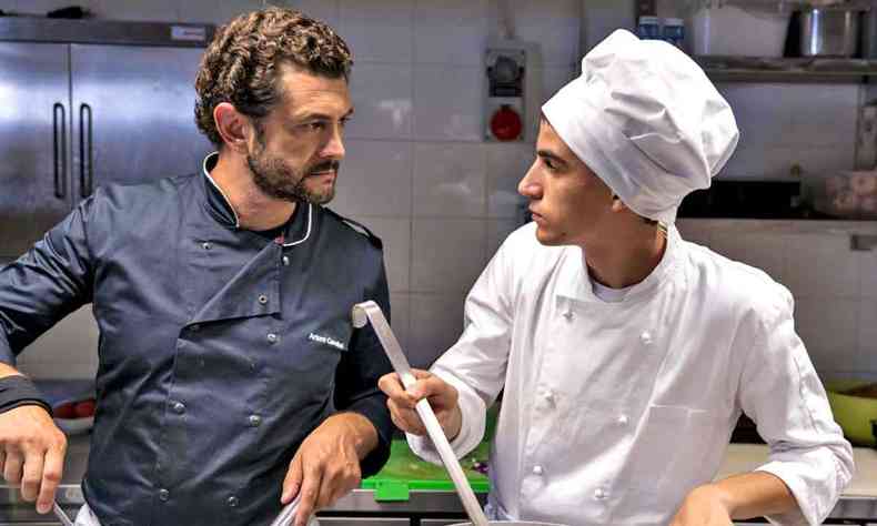 Os atores Vinicio Marchioni e Luigi Fedele se olham enquanto cozinham no filme 'Tempero de chef'