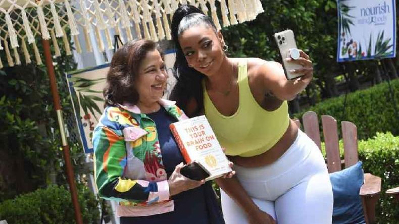 Uma Naidoo (segurando seu livro) e f tiram selfie sorrindo em rea de jardim