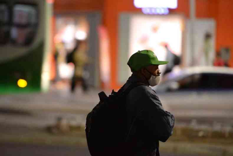 Homem de bon, mscara de proteo e mochila nas costas olha para o lado com fundo desfocado da cidade