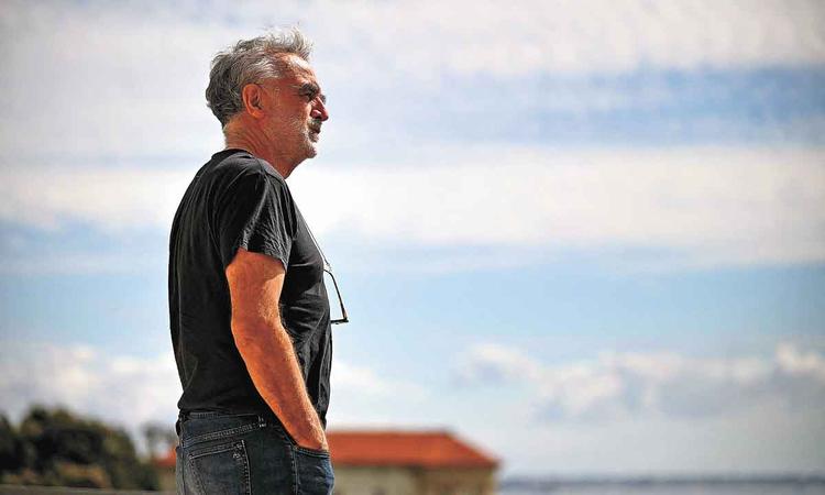Luis Moreno Ocampo, vestido de preto, de pé, ao ar livre, observa a paisagem