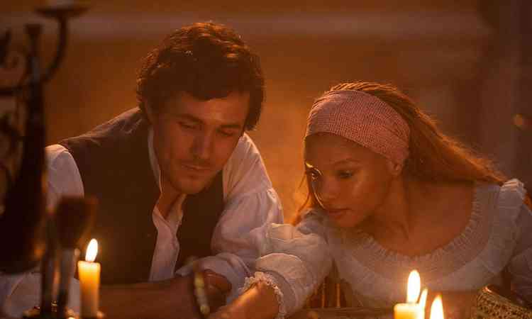 Atores Jonah Hauer-King e Halle Bailey contracenam  luz de velas no filme A pequena sereia