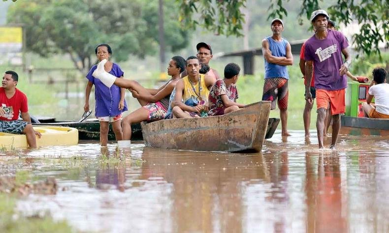 Moradores caminham em trecho alagado da BR-415, entre Itabuna e Ilhéus, enquanto outros usam canoa para atravessar rua inundada Canoa para atravessar rua inundada
