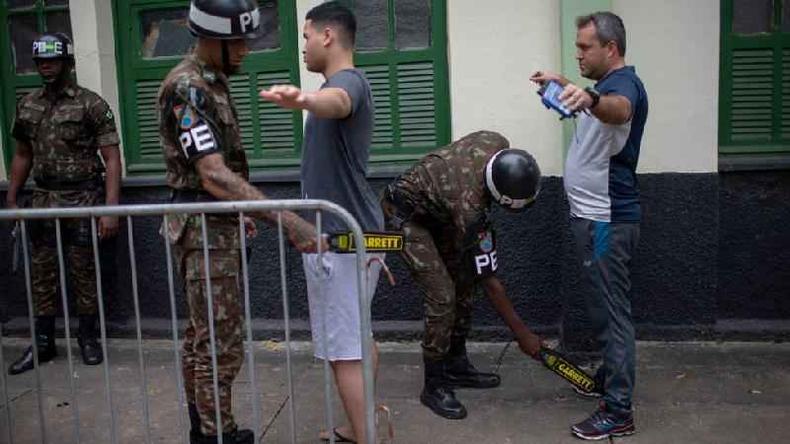 Policiais passam detectores de metais perto dos corpos de dois homens, do lado de fora de uma construo