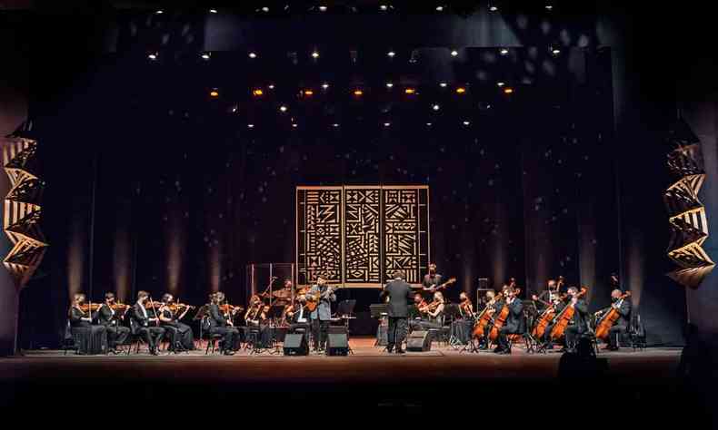 Em cima do palco e diante da orquestra ouro preto, o maestro Rodrigo Toffolo rege os msicos 