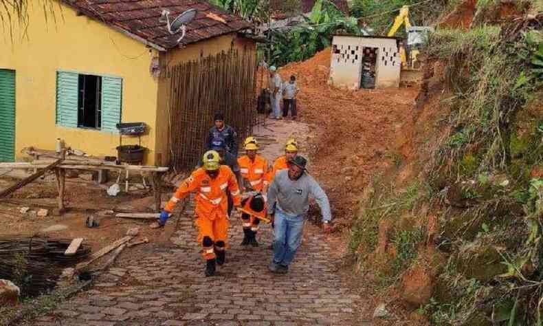 Imagem mostra dois bombeiros carregando homem imobilizado aps deslizamento de terra