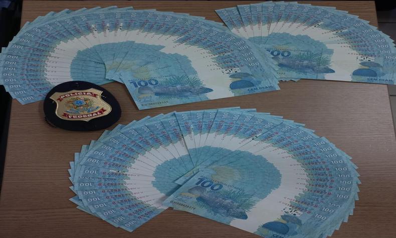 Os oficiais se depararam com a quantia de R$ 10 mil em cédulas falsificadas(foto: Divulgação/Polícia Federal) Dinheiro apreendido dispostos em forma de leques ao lado de distintivo