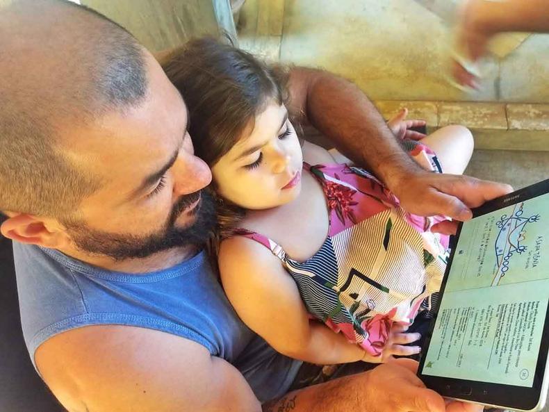 Pai segura criana no colo e mostra a ela aplicativo de leitura exibido no tablet