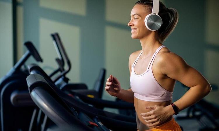 mulher corre na esteira em uma academia com fone com fisionomia feliz