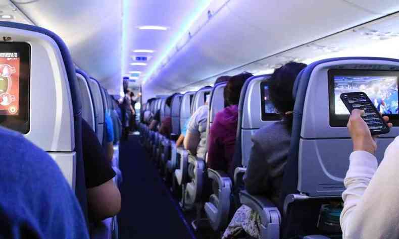 Interior de avio. Viso de costas, pegando o corredor, as poltronas e as pessoas sentadas