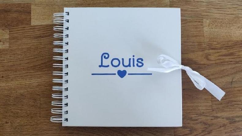 Um lbum de fotos em espiral branco com o nome Louis escrito em azul