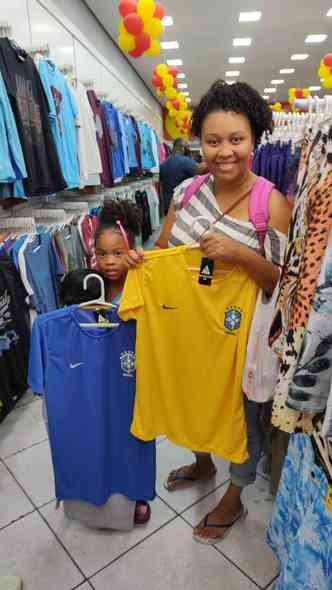 Viviane, mulher negra, com a filha ao lado, segurando uma camisa amarela e outra azul da Seleo Brasileira.