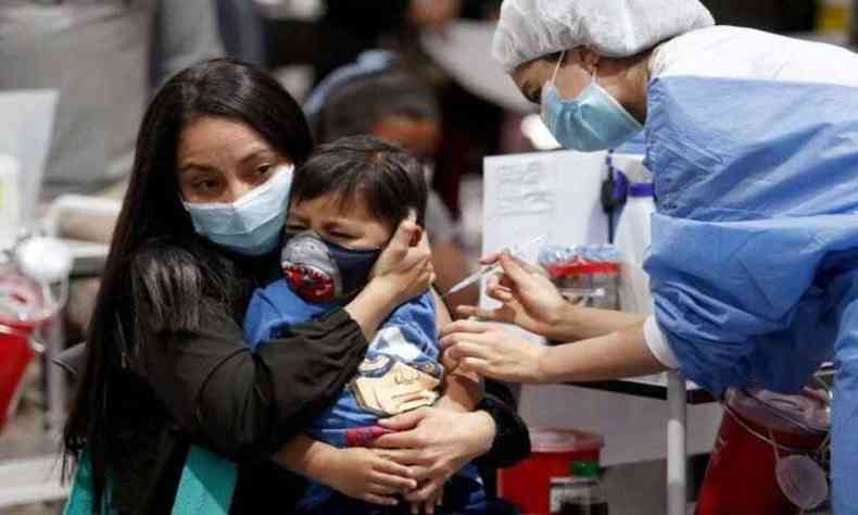 Profissional de saúde aplica vacina em crianças no colo da mãe