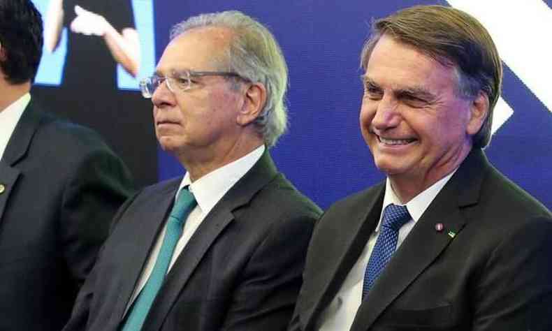 Guedes senta ao lado de Bolsonaro que sorri para fotos