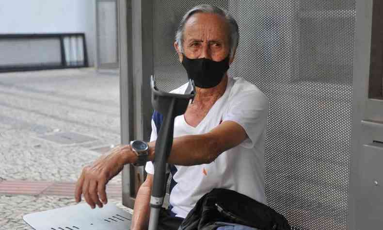 Aposentado Jos Souza, 81 anos, espera nibus sentado com brao apoiado em uma muleta