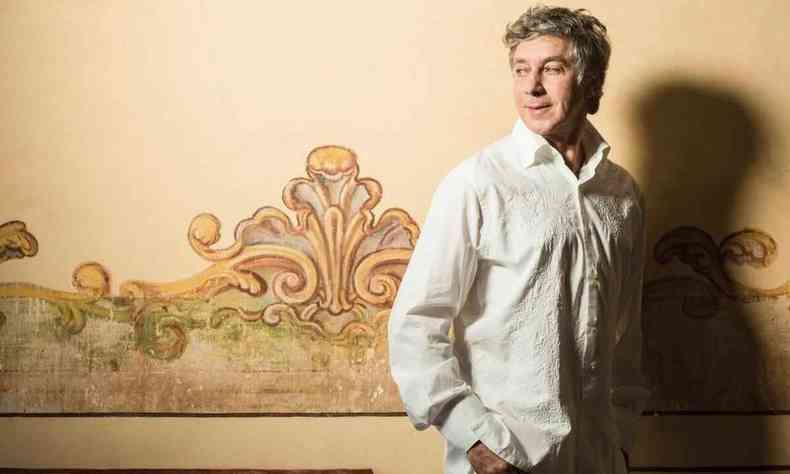 Músico Flavio Venturini posa em frente a parede pintada com motivos que remetem ao barroco colonial minero