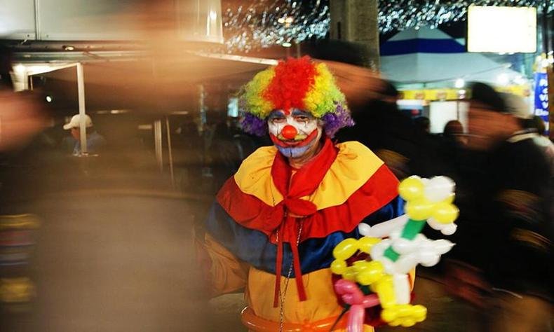 Palhao caracterizado, com roupas coloridas, peruca, nariz vermelho e rosto pintado, mas com semblante triste.