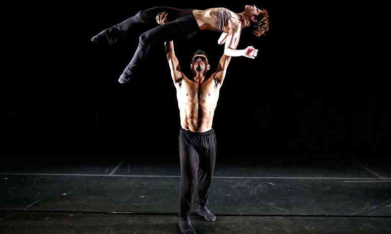 vestindo malha preta, bailarino ergue corpo de bailarina na posio horizontal no palco, segurando-a sobre a cabea, com as duas mos 