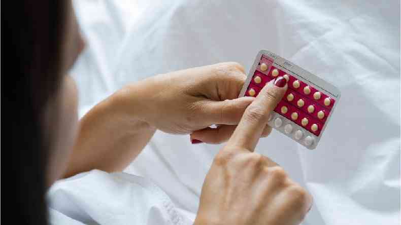 Mulher observa cartela com plulas anticoncepcionais