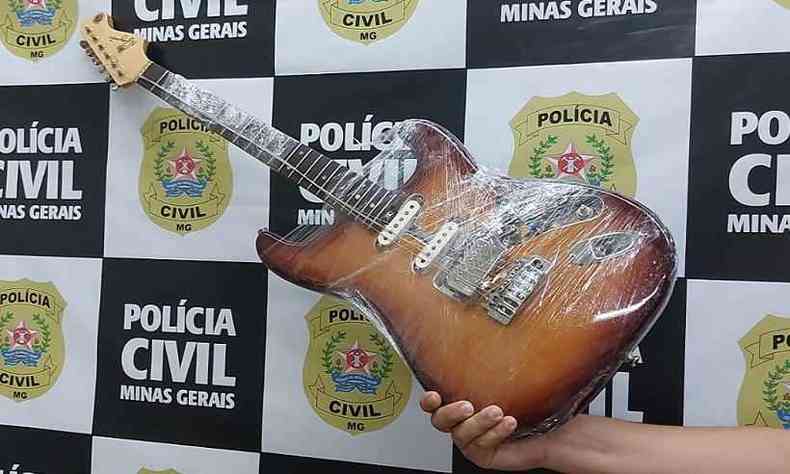 Guitarra em tons de laranja; ao fundo uma parede com o braso da Polcia Civil de Minas Gerais