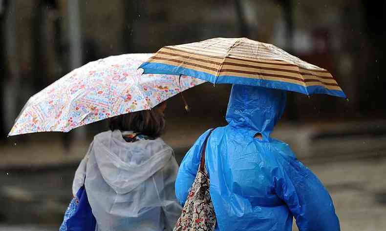 Pessoas com blusas de frio usando sombrinhas para se proteger da chuva