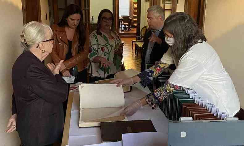 Funcionária da Academia Mineira de Letras, usando luvas, abre livro antigo e o exibe a visitantes